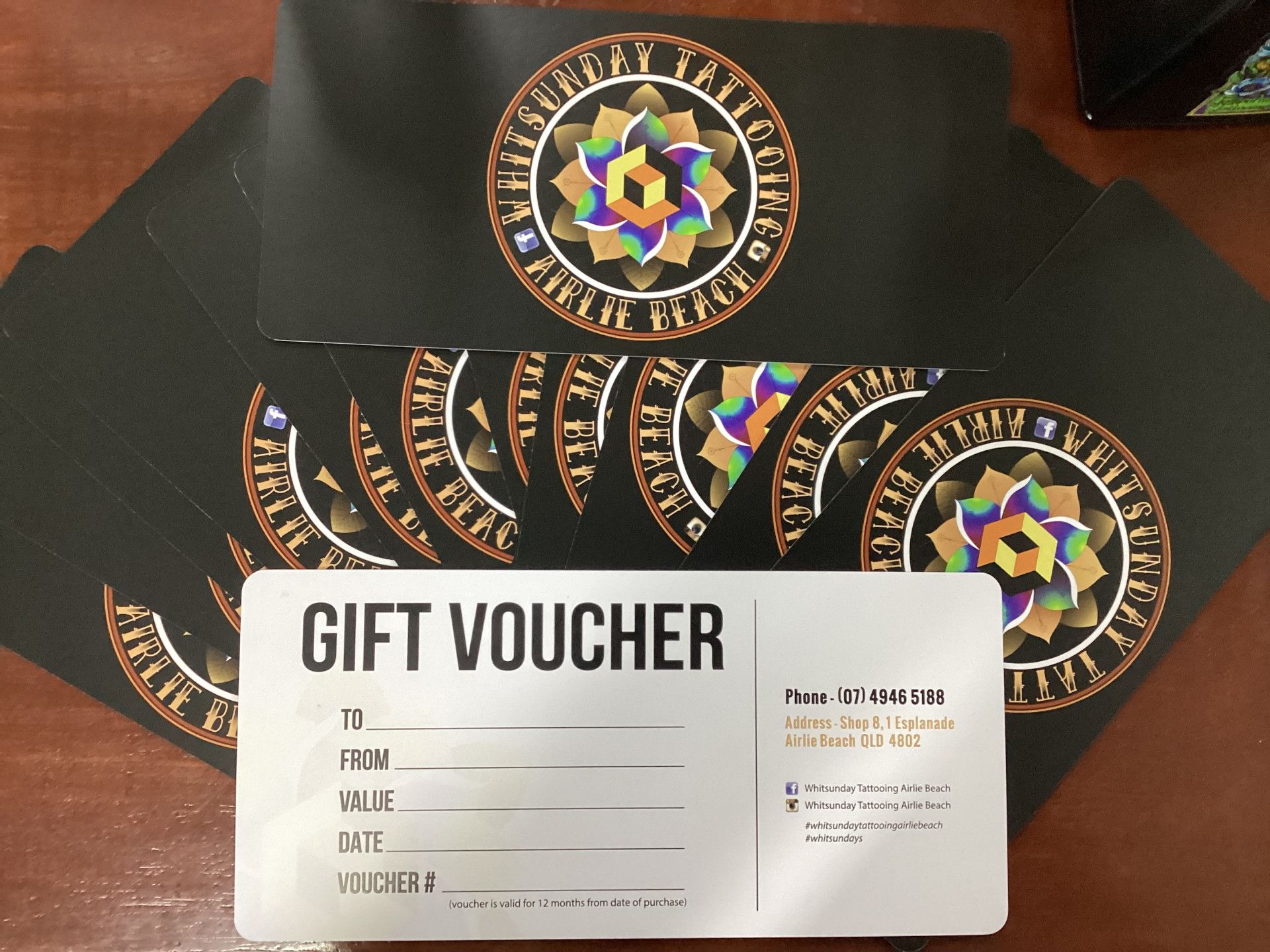 Gift Vouchers on A Table, Black with A Colorful Logo — Whitsunday Tattooing Airlie Beach in Airlie Beach, QLD