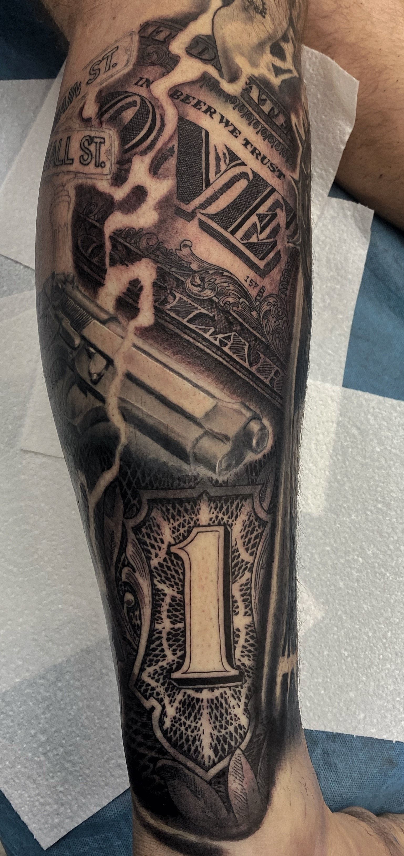 Tattoo of a money-themed design on a person's leg. It features a dollar bill, the number 1, and other currency elements. — Whitsunday Tattooing Airlie Beach in Whitsundays, QLD