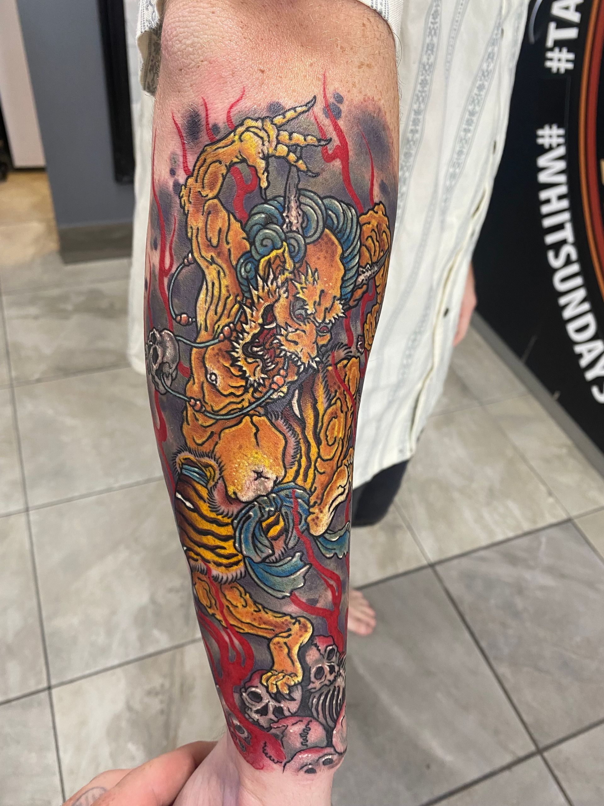 Arm tattoo of a yellow and blue mythical creature with a red background and skull details. — Whitsunday Tattooing Airlie Beach in Whitsundays, QLD