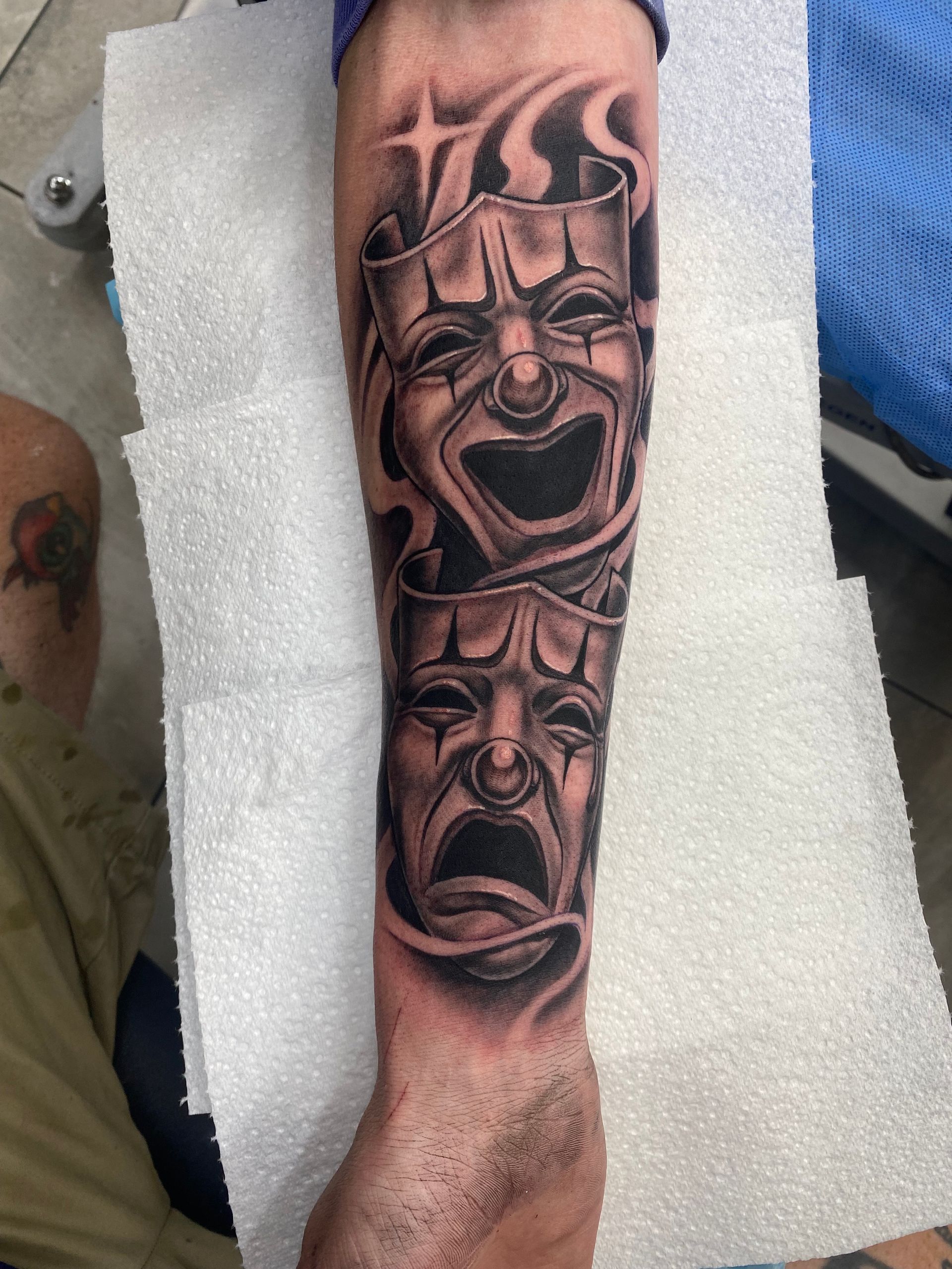 Tattoo of two theatrical masks, one smiling, one frowning, on an arm, with smoky background. — Whitsunday Tattooing Airlie Beach in Whitsundays, QLD