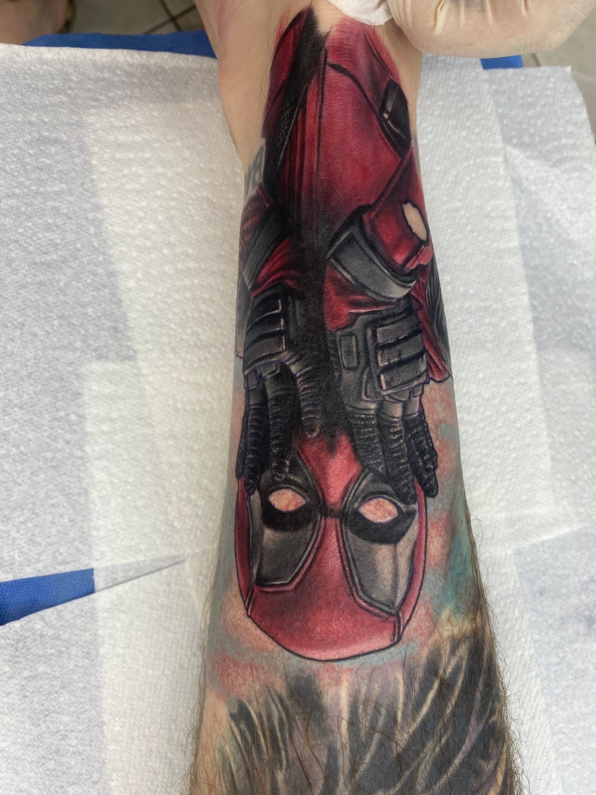 Deadpool tattoo on a person's forearm, showing the character's mask and costume in red and black. — Whitsunday Tattooing Airlie Beach in Whitsundays, QLD
