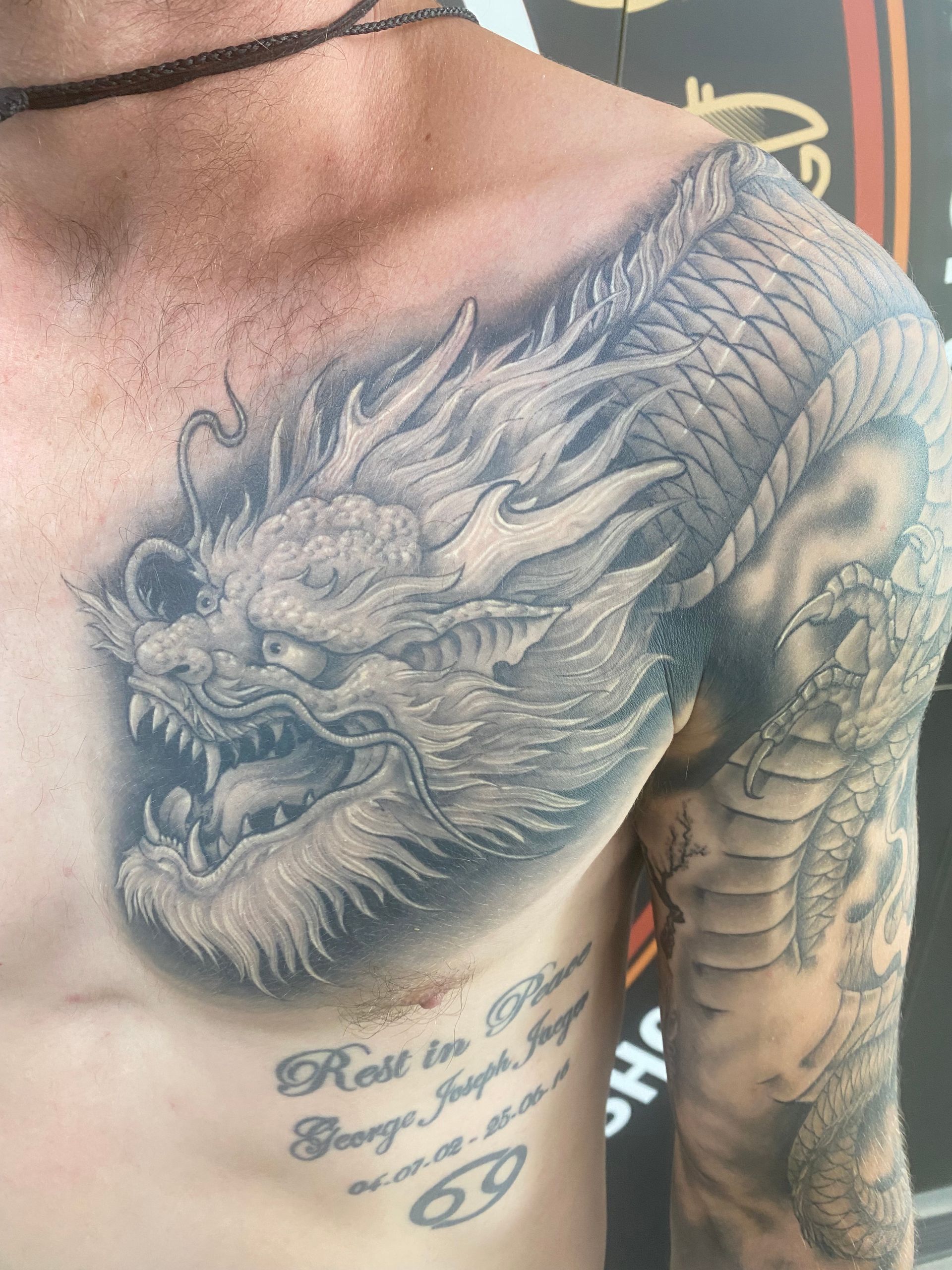 Tattoo of a grey dragon on a person's chest and shoulder. Includes writing below chest. — Whitsunday Tattooing Airlie Beach in Whitsundays, QLD