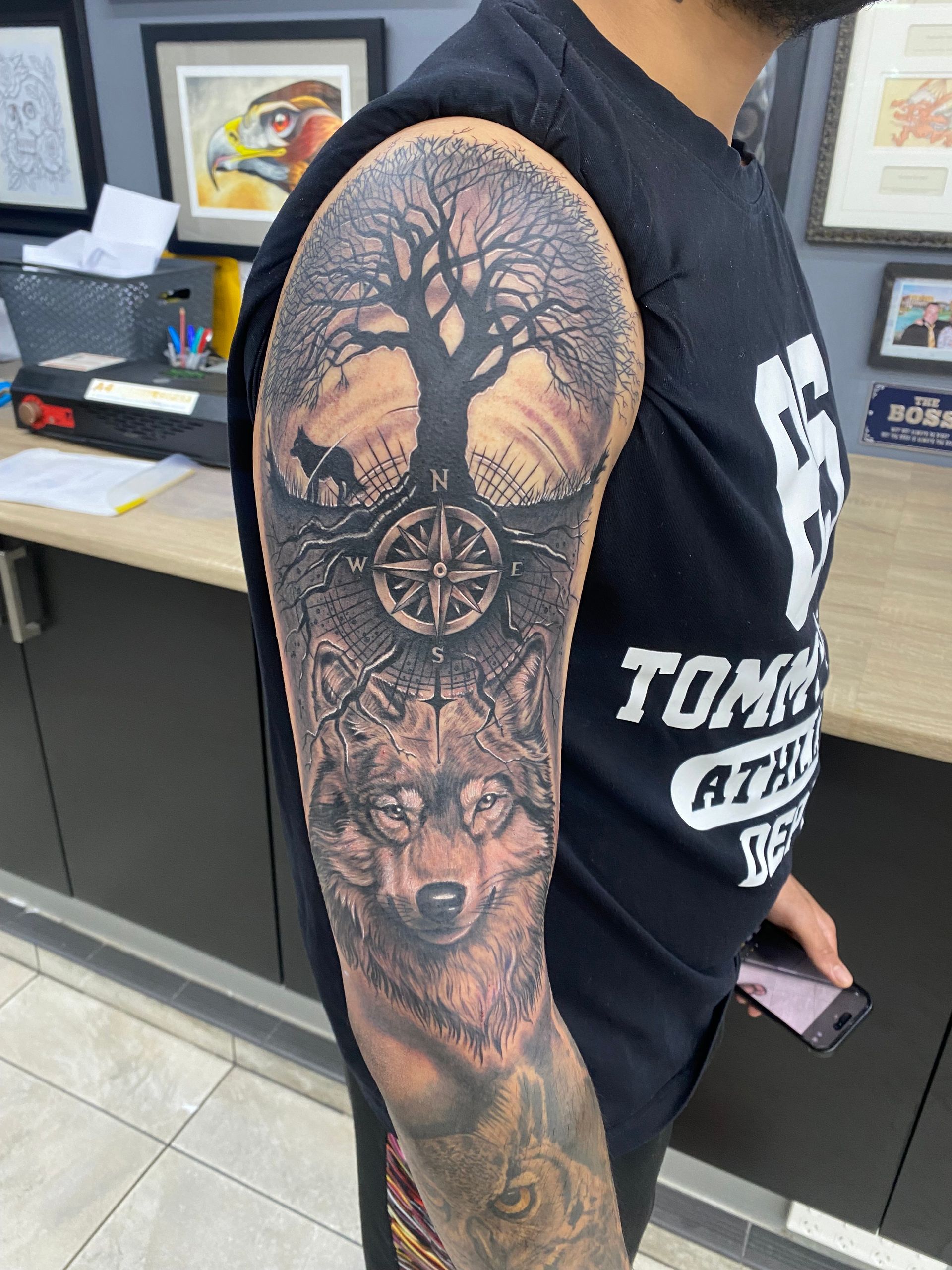 Man with a detailed wolf and tree arm tattoo. In a tattoo parlor setting, wearing a black shirt and holding a phone. — Whitsunday Tattooing Airlie Beach in Whitsundays, QLD