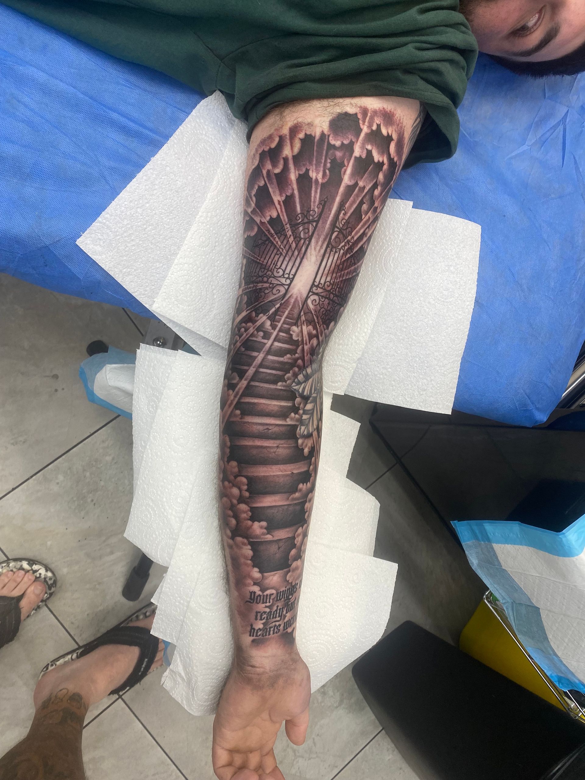 Tattoo of a staircase with light rays on an arm. Person in green shirt lies on a blue surface. — Whitsunday Tattooing Airlie Beach in Whitsundays, QLD