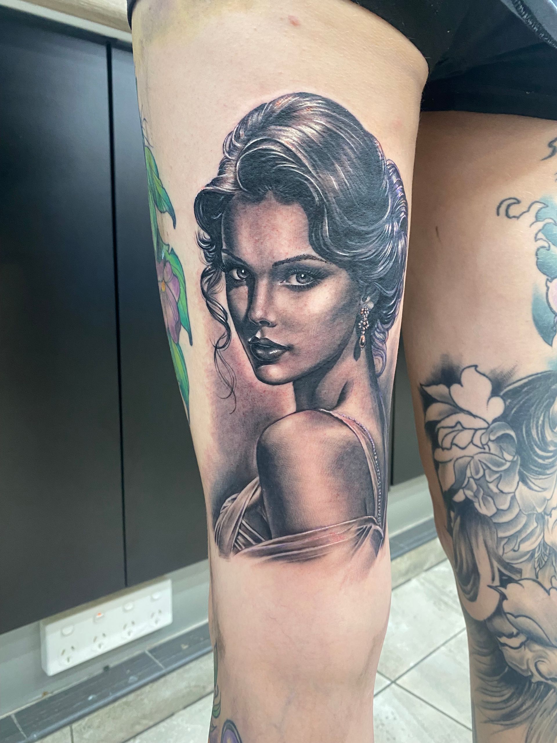 Tattoo of a woman's portrait in grayscale on a leg. The woman is looking over her shoulder with a serious expression. — Whitsunday Tattooing Airlie Beach in Whitsundays, QLD