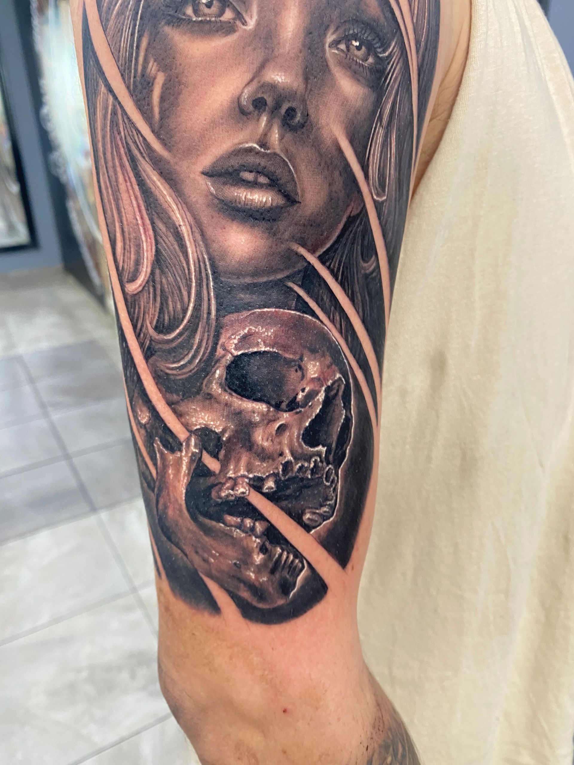 Tattoo on arm, woman's face above skull. Black and grey ink, detailed shading, light streaks. — Whitsunday Tattooing Airlie Beach in Whitsundays, QLD