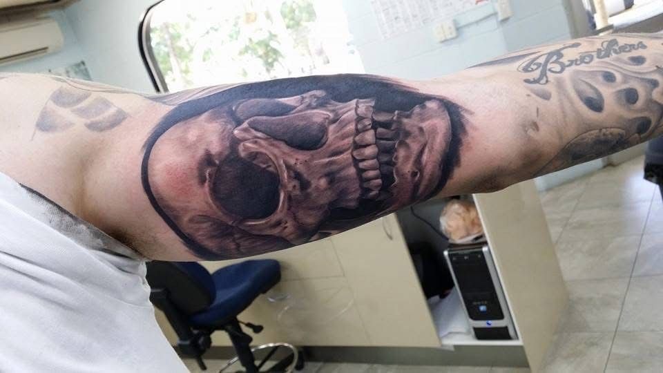 Skull tattoo on a person's upper arm, with detailed shading and realistic look. The setting appears to be a tattoo studio. — Whitsunday Tattooing Airlie Beach in Whitsundays, QLD