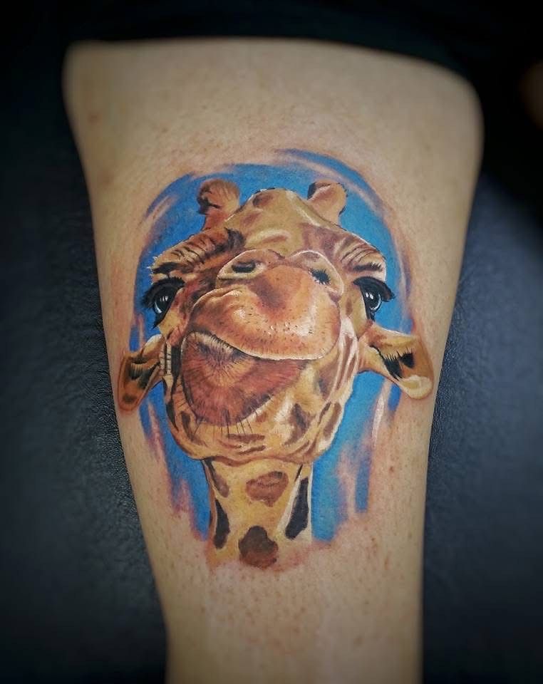 Giraffe face tattoo with a blue background; the giraffe is smiling. — Whitsunday Tattooing Airlie Beach in Whitsundays, QLD