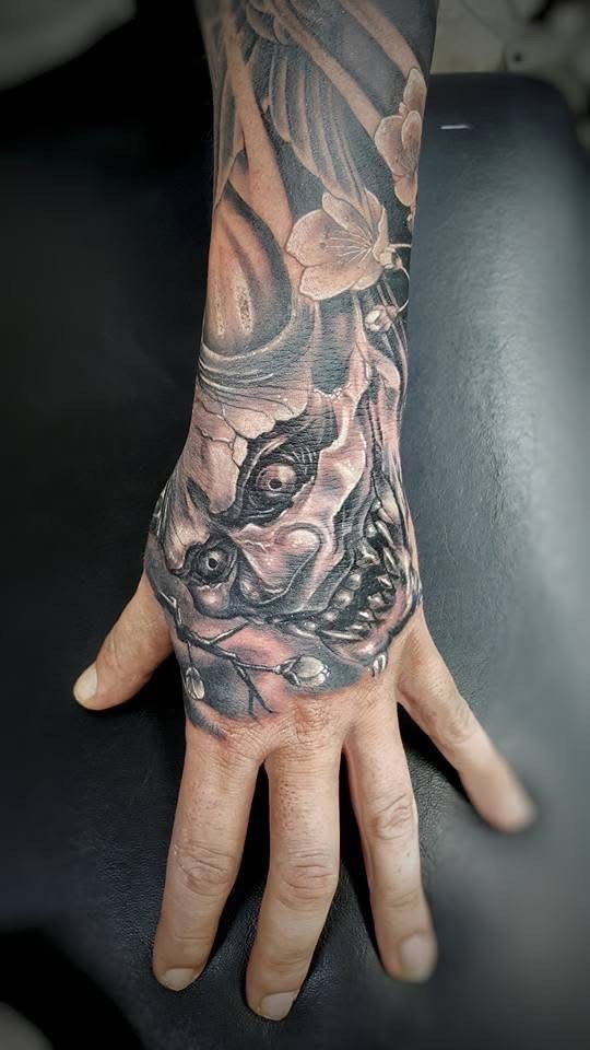 Hand with a detailed black and gray tattoo of a face, possibly a monster, with floral elements extending up the forearm. — Whitsunday Tattooing Airlie Beach in Whitsundays, QLD