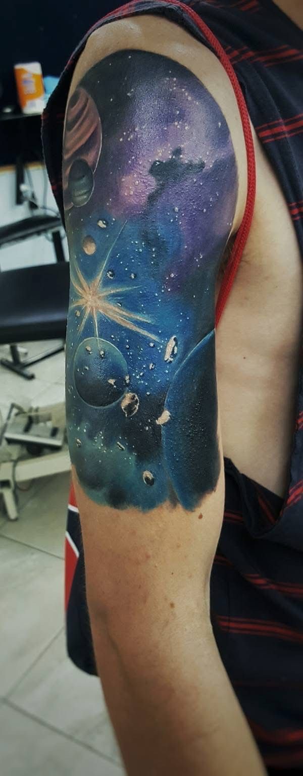 Tattoo of a galaxy on a person's upper arm. Features planets, stars, and nebulas in shades of blue and purple. — Whitsunday Tattooing Airlie Beach in Whitsundays, QLD