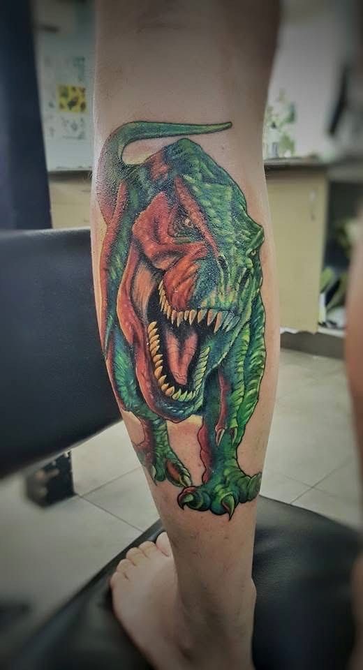 Color tattoo of a Tyrannosaurus Rex on a person's leg, roaring with an open mouth and sharp teeth. — Whitsunday Tattooing Airlie Beach in Whitsundays, QLD
