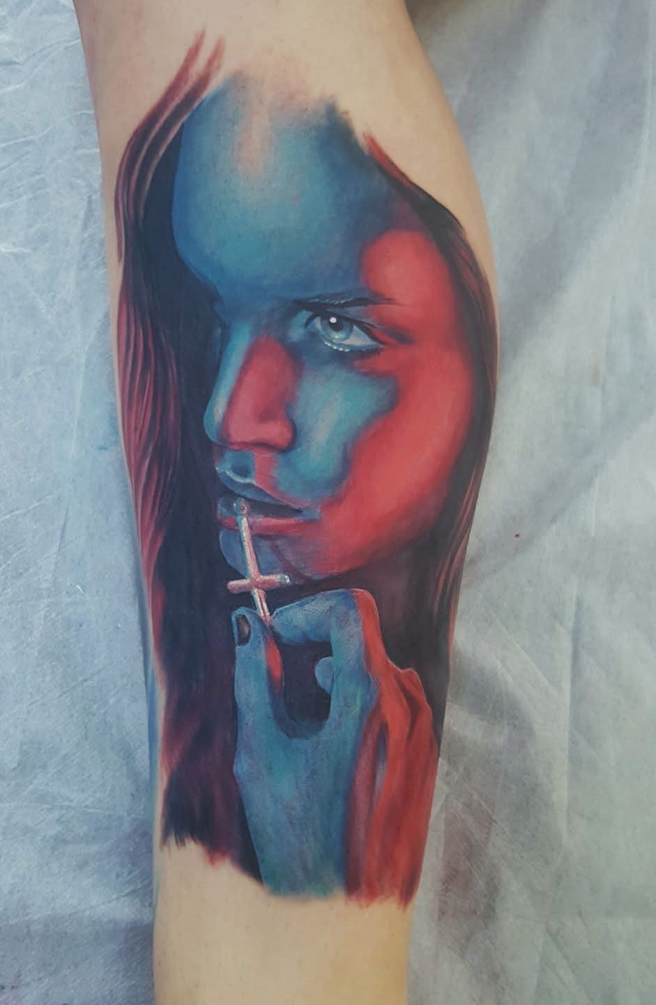 Tattoo of a woman in blue and red tones, holding a cross pendant, gazing pensively. — Whitsunday Tattooing Airlie Beach in Whitsundays, QLD