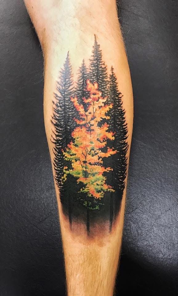 Tattoo of a forest scene on a leg. Black evergreen trees surround a central tree with orange and green leaves. — Whitsunday Tattooing Airlie Beach in Whitsundays, QLD