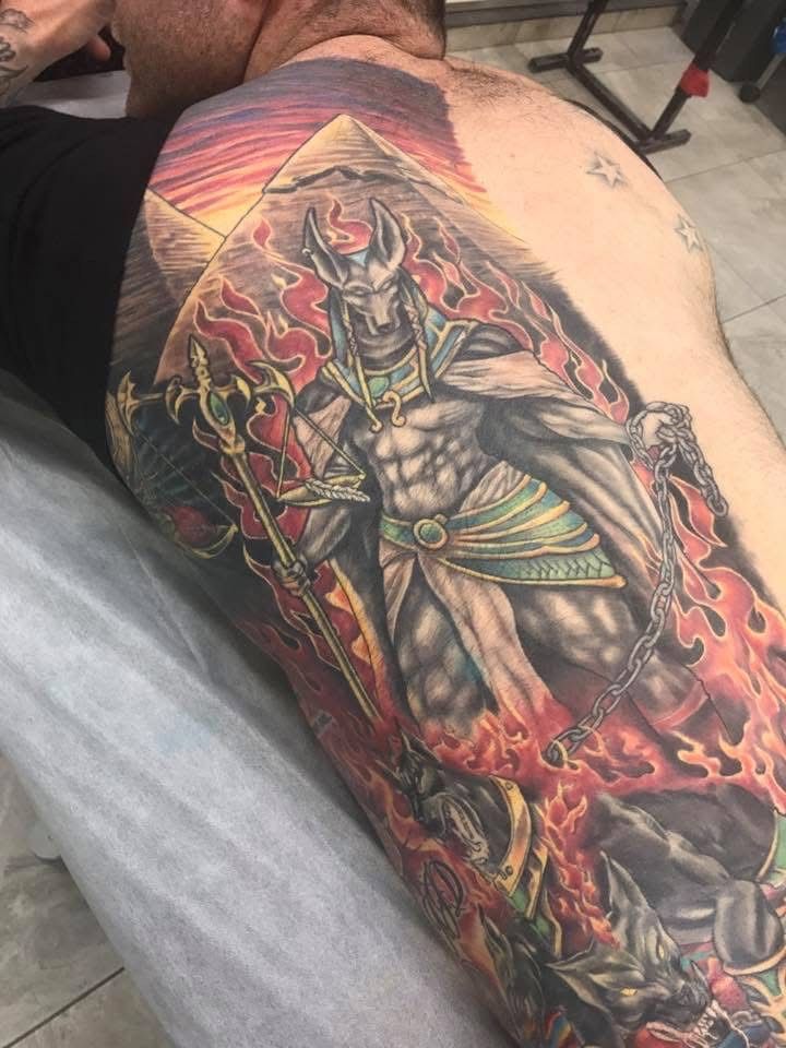 Tattoo of Anubis with flames, staff, and chain on a person's upper arm and back. Includes pyramids and sunset colors. — Whitsunday Tattooing Airlie Beach in Whitsundays, QLD