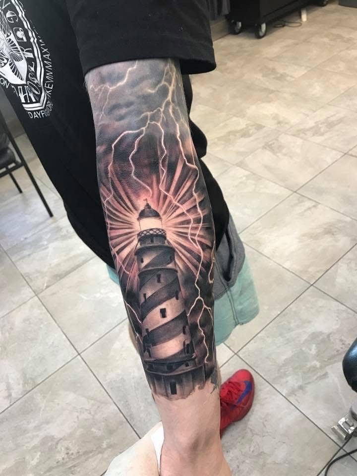 Tattoo of a lighthouse shining bright light against a stormy sky on a person's arm. — Whitsunday Tattooing Airlie Beach in Whitsundays, QLD