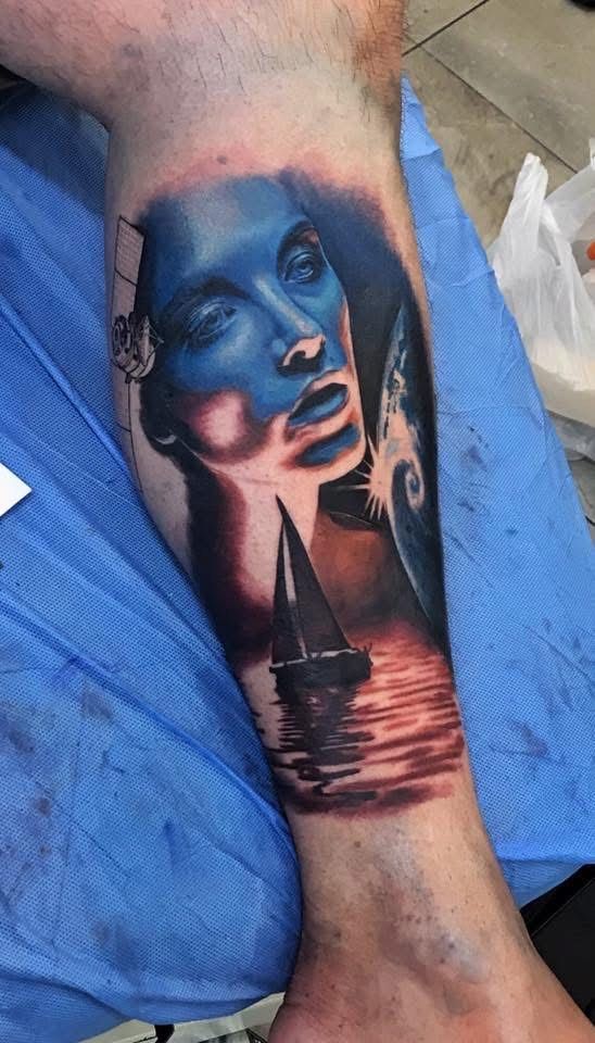 Blue-toned woman's face and sailboat tattoo on an arm, with a sunset scene. — Whitsunday Tattooing Airlie Beach in Whitsundays, QLD