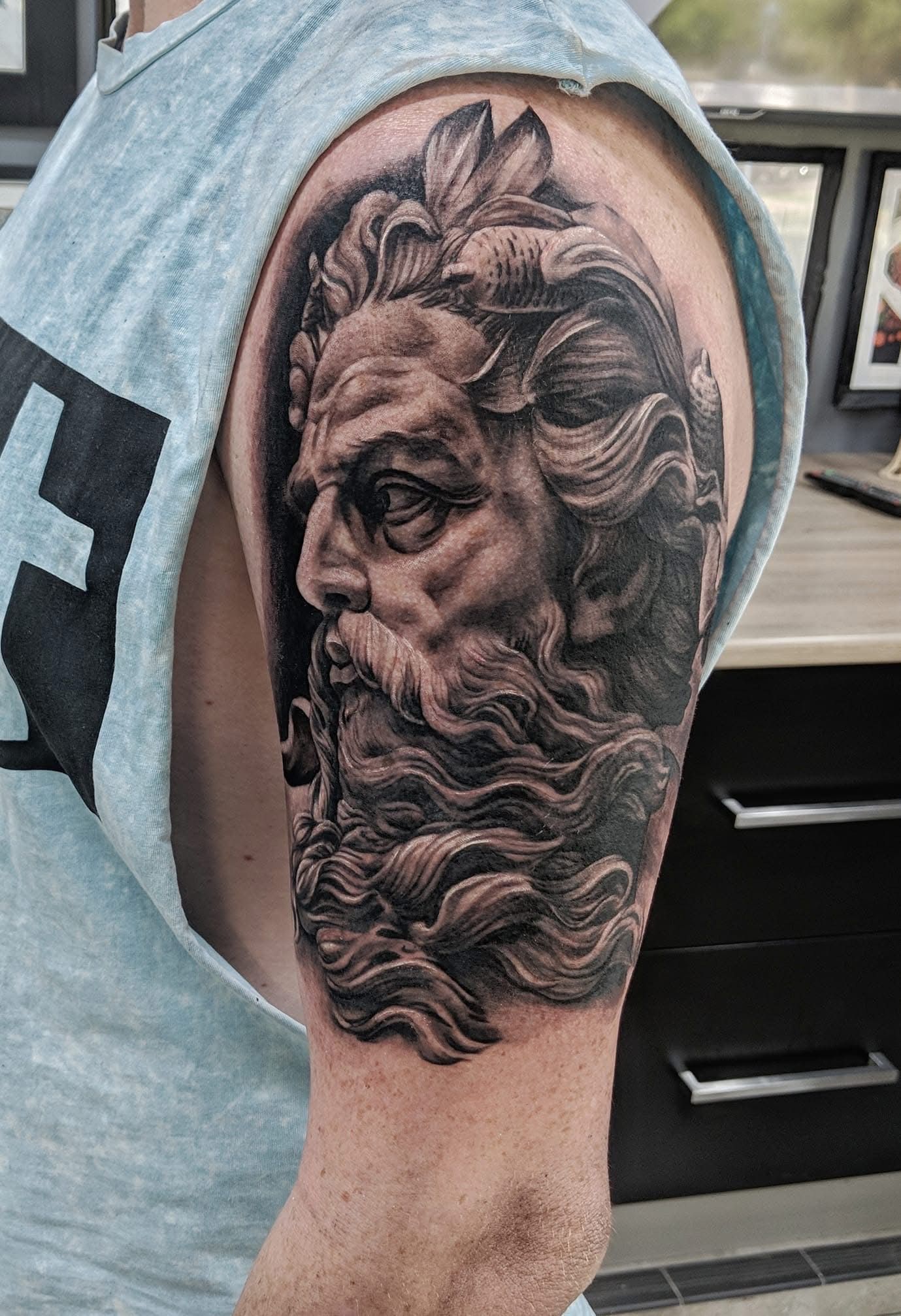 Tattoo of a bearded man's bust, likely Zeus or Poseidon, on a person's upper arm. Black and gray, detailed shading. — Whitsunday Tattooing Airlie Beach in Whitsundays, QLD