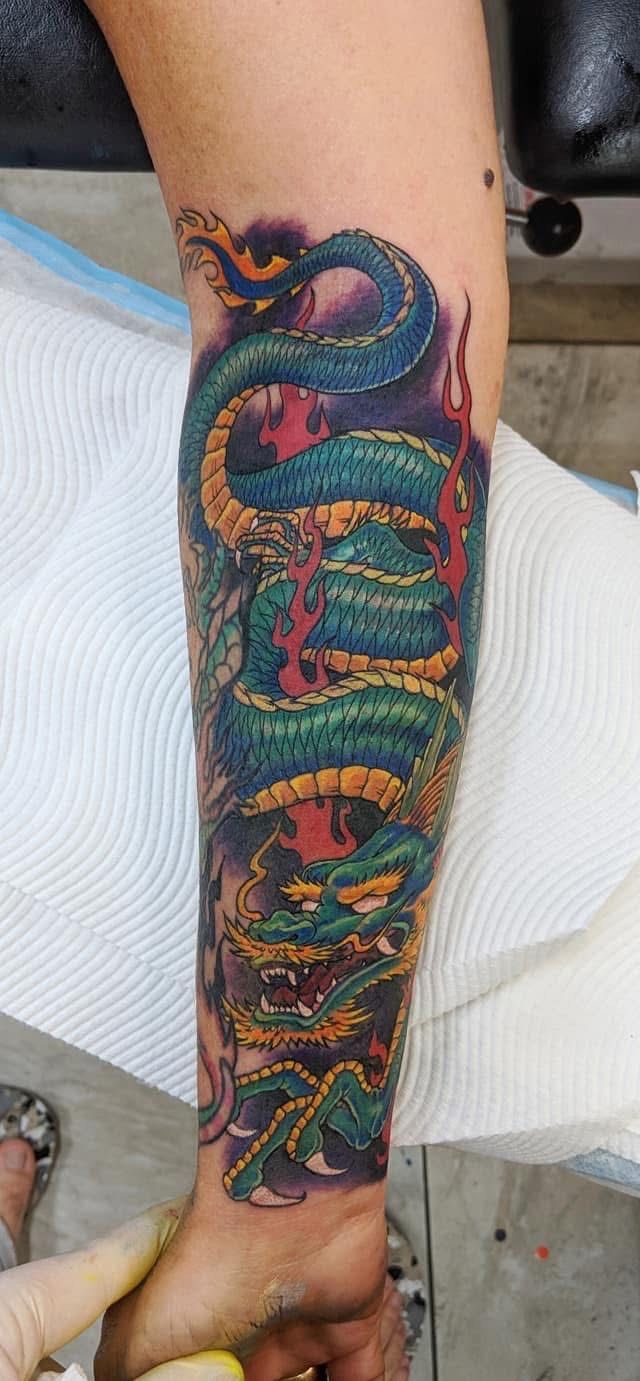 Detailed colorful dragon tattoo on an arm, showing green, blue, yellow, and red scales against dark background. — Whitsunday Tattooing Airlie Beach in Whitsundays, QLD