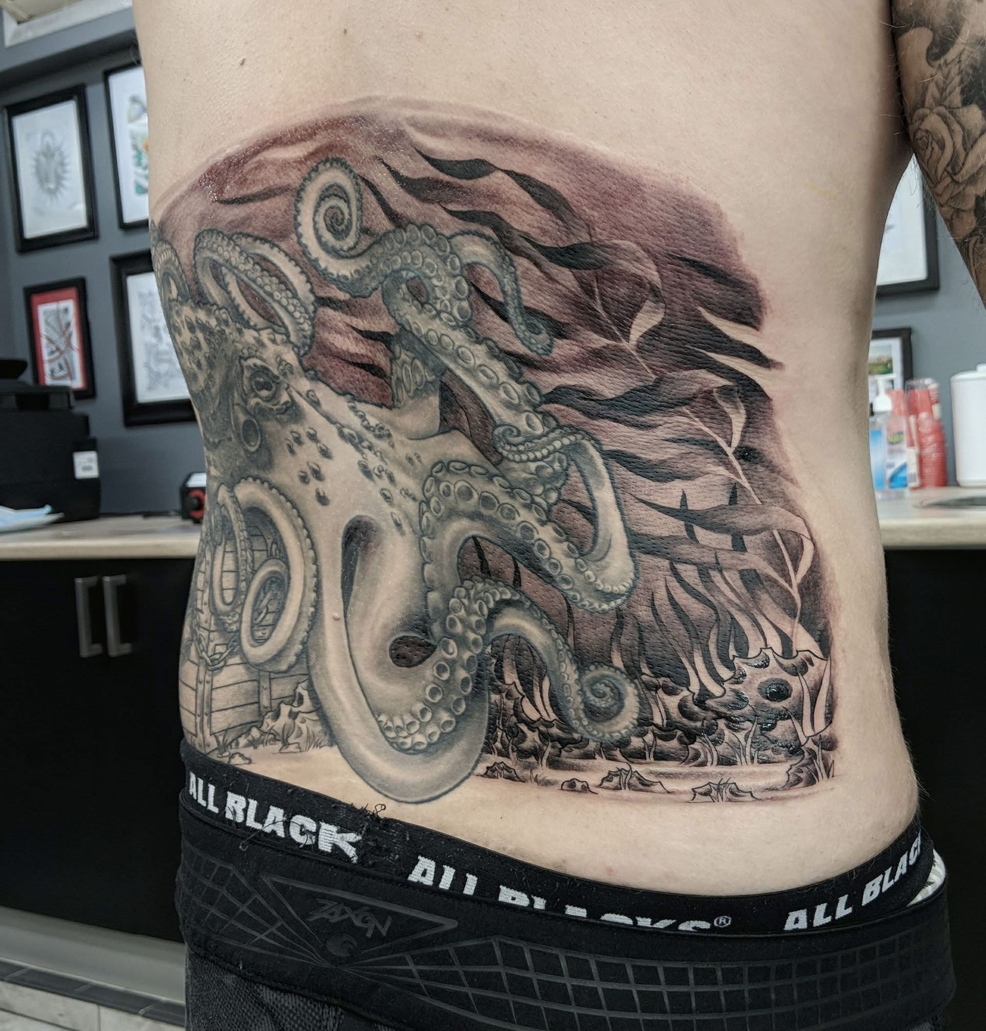 Tattoo of an octopus on a person's side, with coral and underwater background. Black and grey ink. — Whitsunday Tattooing Airlie Beach in Whitsundays, QLD