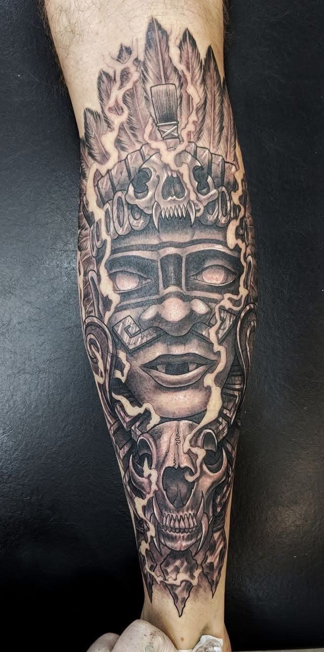 A black and gray leg tattoo featuring a detailed Aztec mask with skulls. — Whitsunday Tattooing Airlie Beach in Whitsundays, QLD