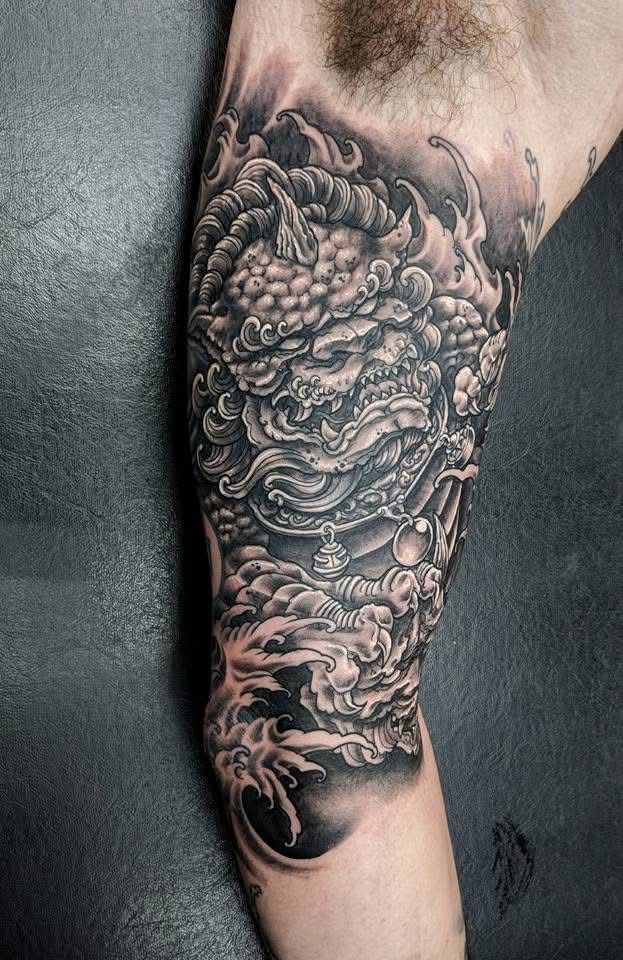 Tattoo of a Foo dog in black and gray, on a person's upper arm. Detailed shading with clouds and swirls. — Whitsunday Tattooing Airlie Beach in Whitsundays, QLD