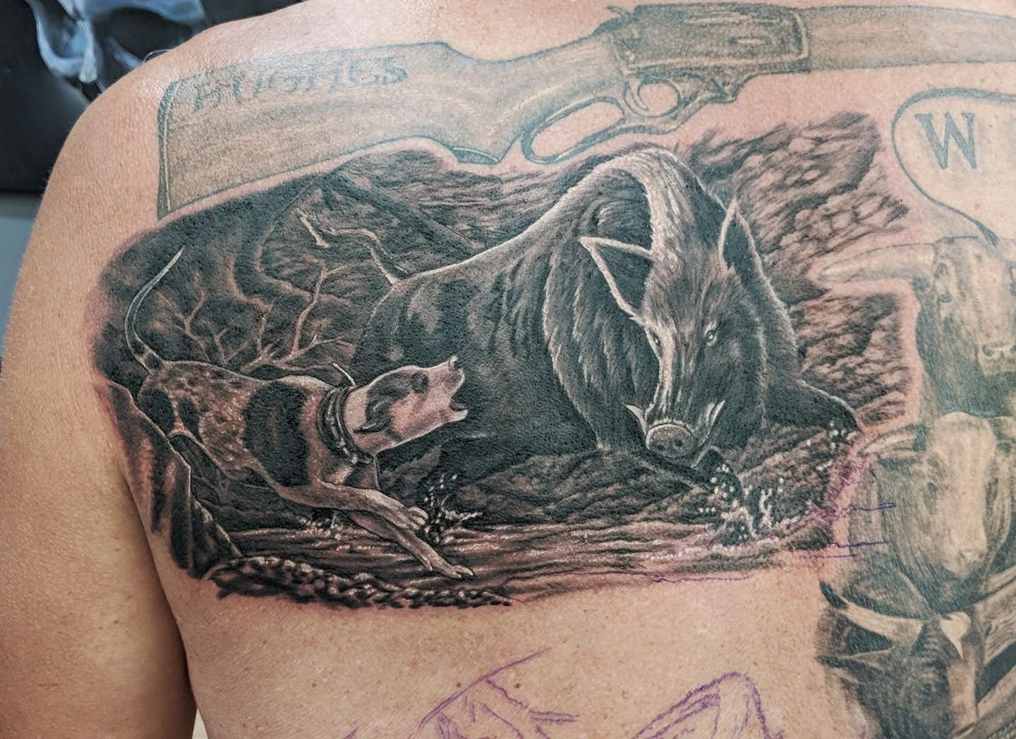 Tattoo of a dog barking at a large animal in a forest setting; a hunting rifle is above the scene. — Whitsunday Tattooing Airlie Beach in Whitsundays, QLD