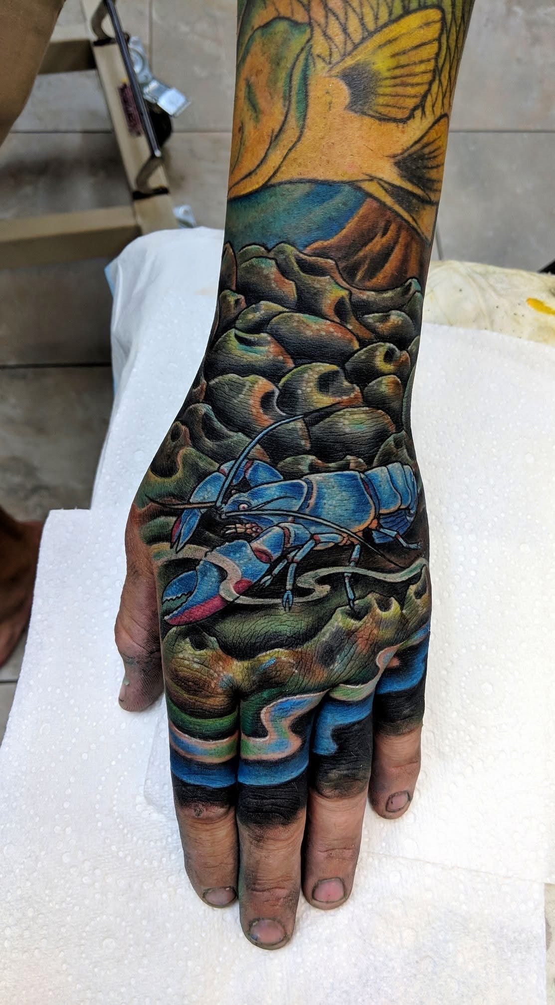 Detailed tattoo of a blue scorpion on a hand, with colorful ocean scene on arm, fingers also inked. — Whitsunday Tattooing Airlie Beach in Whitsundays, QLD