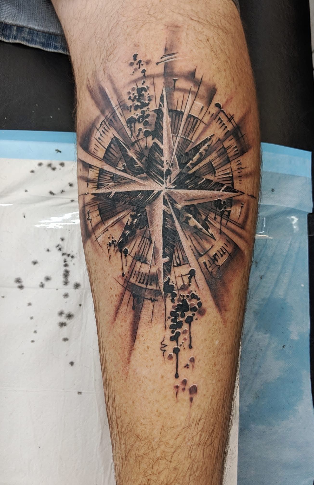 Tattoo of a compass rose on a leg, with radial lines, roman numerals, and shaded details in black and gray. — Whitsunday Tattooing Airlie Beach in Whitsundays, QLD