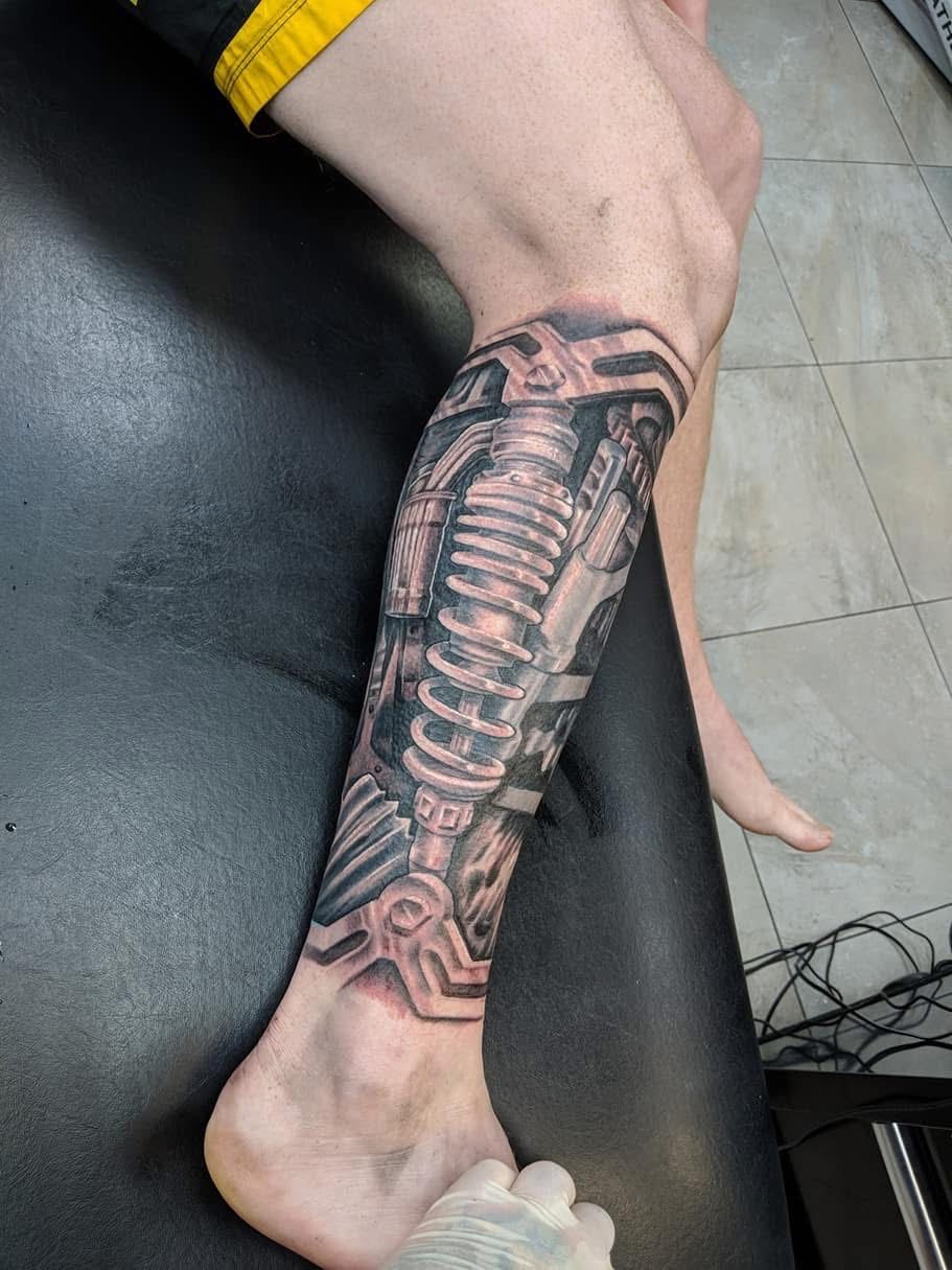 Tattoo of a mechanical leg on a person's calf in black and gray ink. Leg is on a black surface. — Whitsunday Tattooing Airlie Beach in Whitsundays, QLD