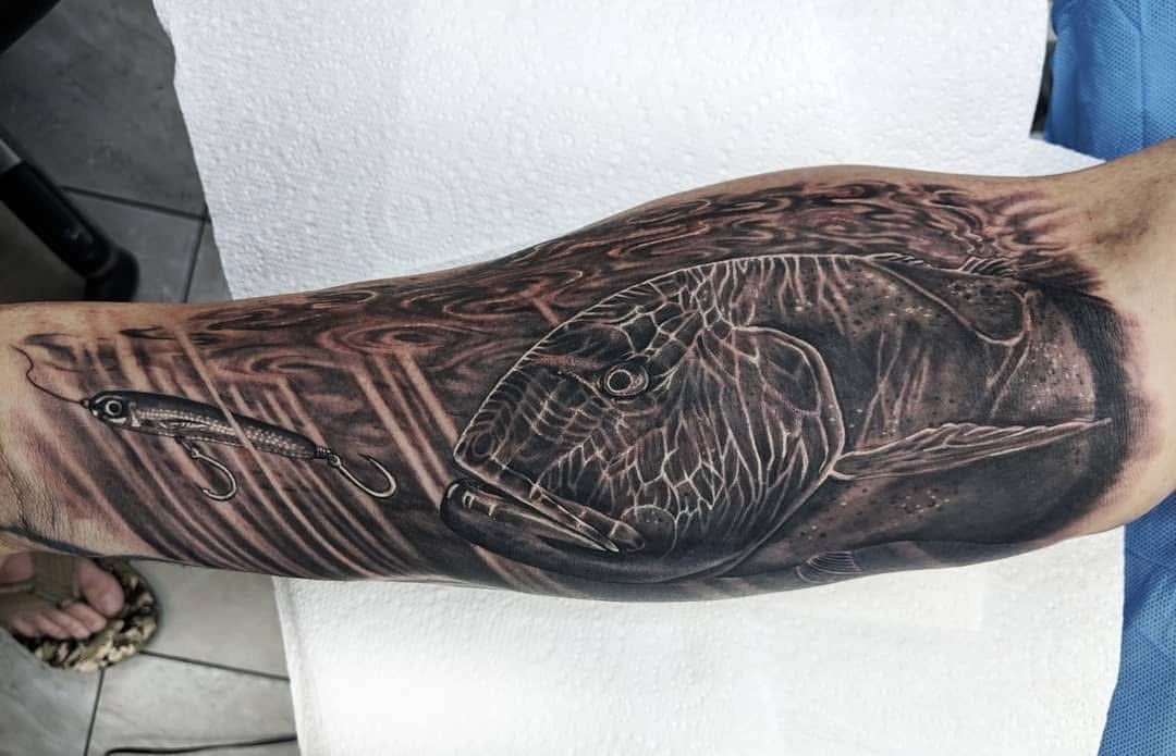 Tattoo of a bird with a fishing lure on an arm, with dark shading. — Whitsunday Tattooing Airlie Beach in Whitsundays, QLD