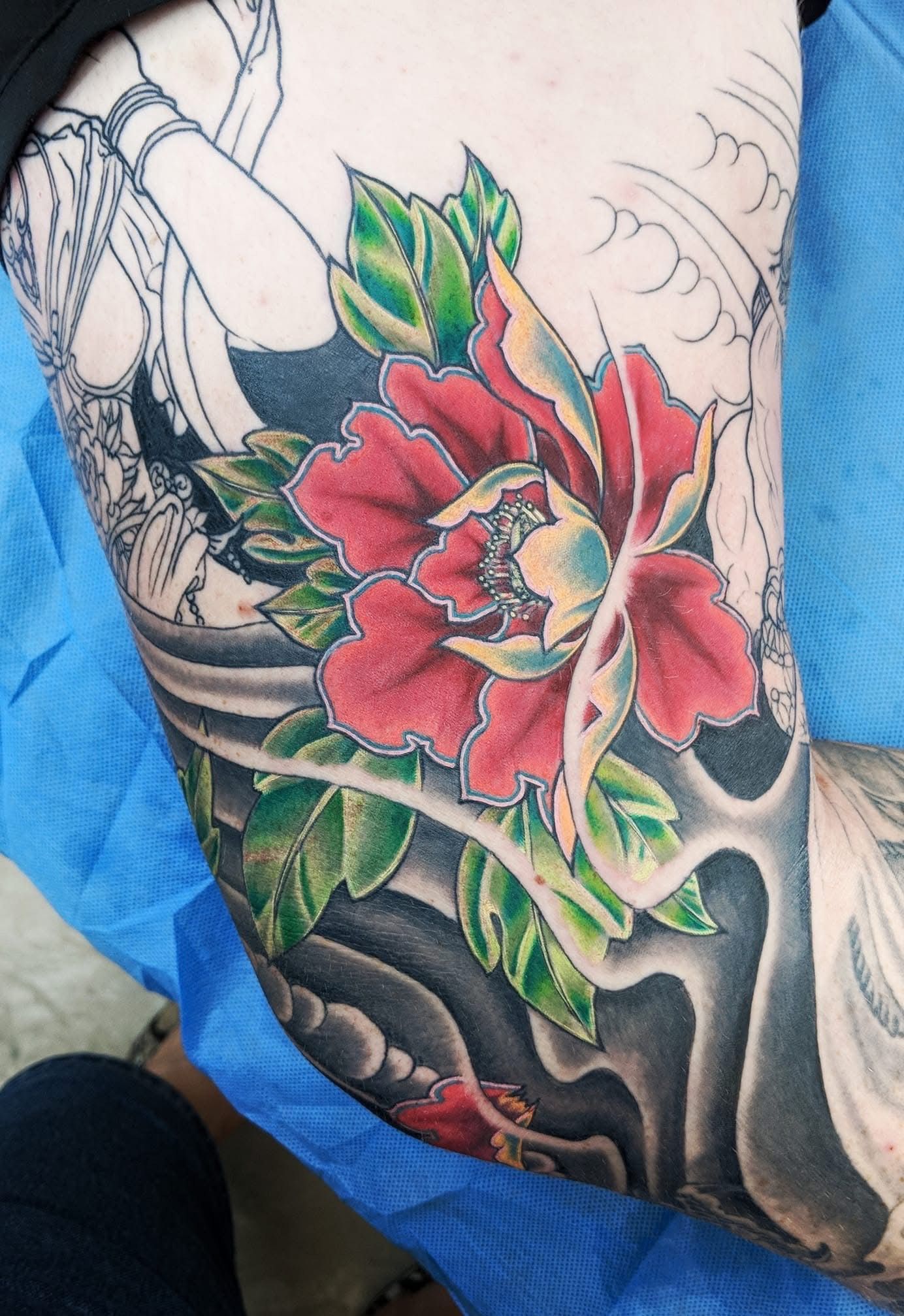 Tattoo of a vibrant red peony flower with green leaves, surrounded by black waves and partial sketch of figures. — Whitsunday Tattooing Airlie Beach in Whitsundays, QLD