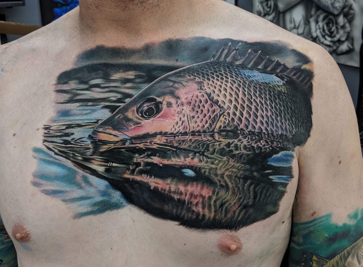 Chest tattoo of a fish surfacing from water with a detailed reflection. — Whitsunday Tattooing Airlie Beach in Whitsundays, QLD