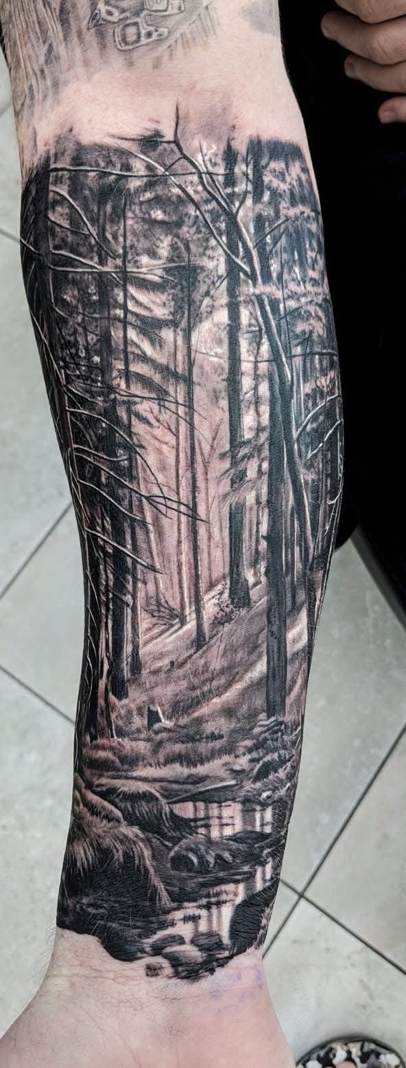 Black and white forest scene tattoo on a forearm. Features trees, a path, and water at the bottom. — Whitsunday Tattooing Airlie Beach in Whitsundays, QLD