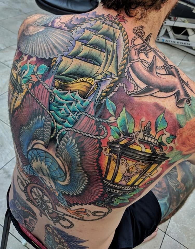 Colorful nautical tattoo on a person's upper back, featuring a ship, waves, birds, anchor, and a lantern. — Whitsunday Tattooing Airlie Beach in Whitsundays, QLD