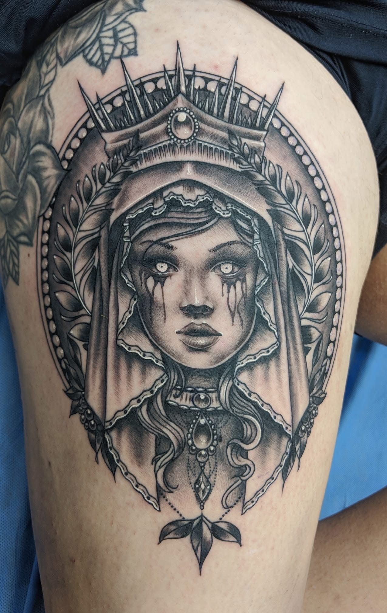 Black and gray tattoo of a woman with a crown and veil, within an ornate circle, on a thigh. — Whitsunday Tattooing Airlie Beach in Whitsundays, QLD