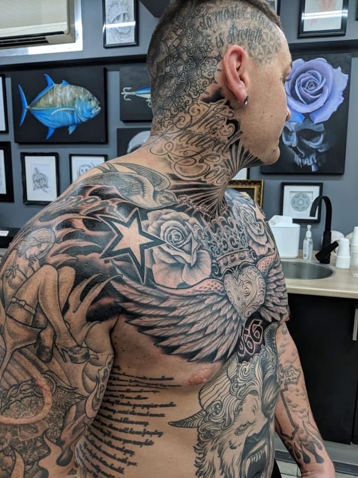 Man with full torso and neck tattoos in a tattoo parlor, featuring stars, roses, and wings. — Whitsunday Tattooing Airlie Beach in Whitsundays, QLD