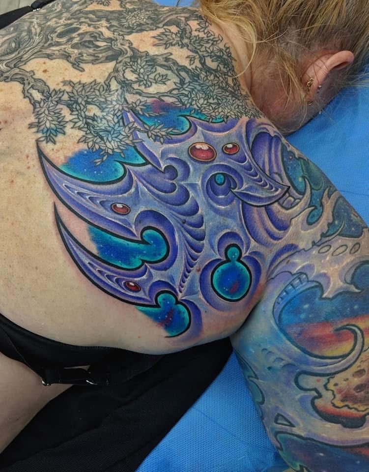 Person with colorful abstract tattoo on back and arm, with blue, purple, and red hues. — Whitsunday Tattooing Airlie Beach in Whitsundays, QLD