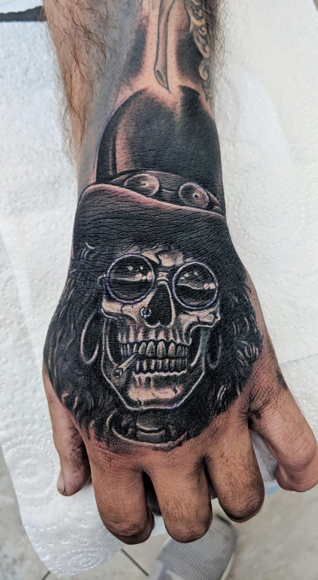 Hand tattoo depicting a skull wearing sunglasses and a top hat, in black and gray ink. — Whitsunday Tattooing Airlie Beach in Whitsundays, QLD