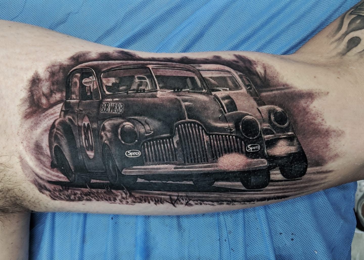 Tattoo of two vintage race cars on a person's arm, shaded in black and gray. — Whitsunday Tattooing Airlie Beach in Whitsundays, QLD