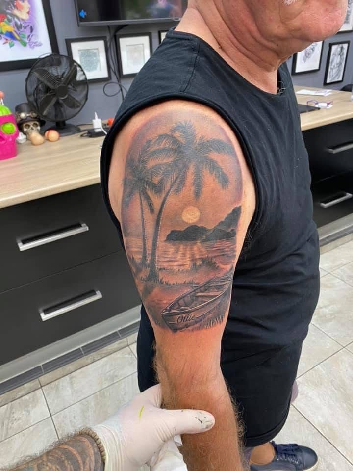 Tattoo of a tropical beach scene on a man's arm. Palm trees, water, and sun in a hazy, grayscale design. — Whitsunday Tattooing Airlie Beach in Whitsundays, QLD
