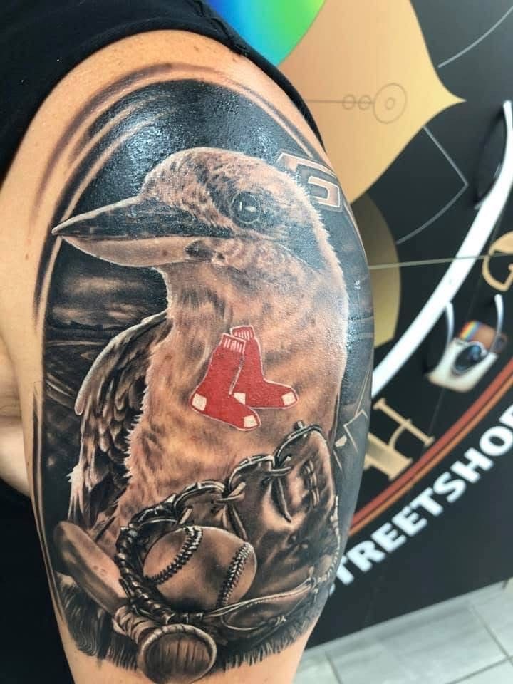 Tattoo of a bird with a baseball glove, baseball, and Red Sox logo on shoulder. Black and gray, with red accents. — Whitsunday Tattooing Airlie Beach in Whitsundays, QLD