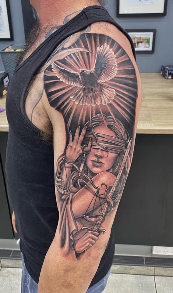 Tattoo of a dove above Lady Justice holding scales and a sword, on a person's upper arm. — Whitsunday Tattooing Airlie Beach in Whitsundays, QLD