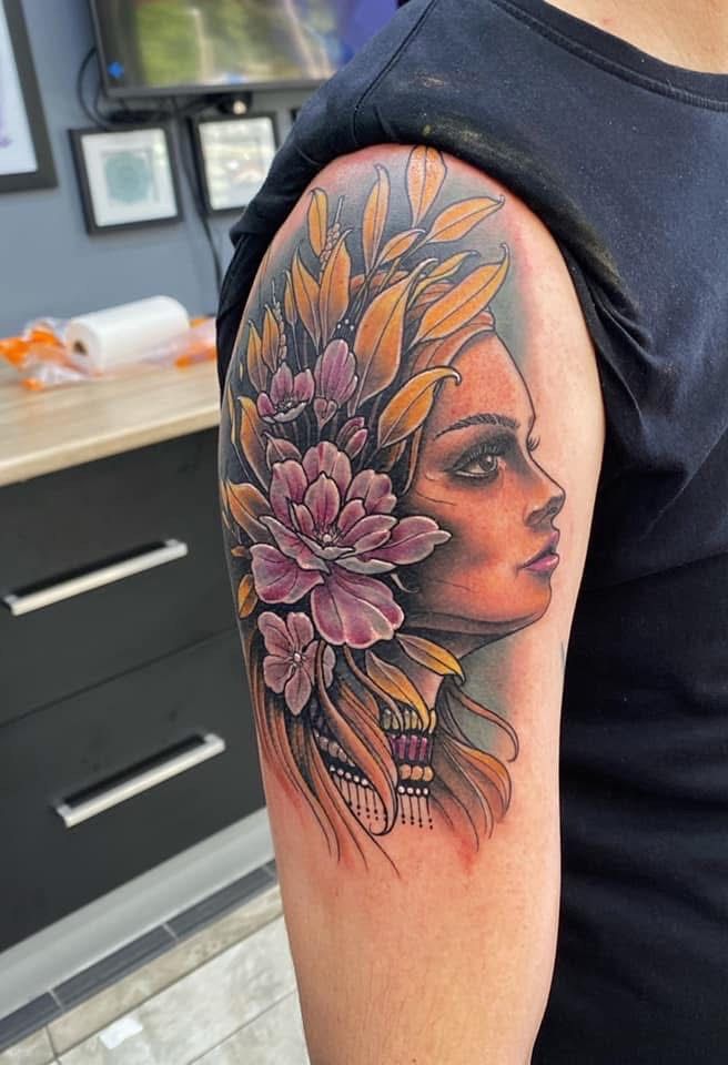 Tattoo of a woman's face with flowers and leaves on a man's arm. The tattoo is colorful, with pink, yellow, and brown tones. — Whitsunday Tattooing Airlie Beach in Whitsundays, QLD