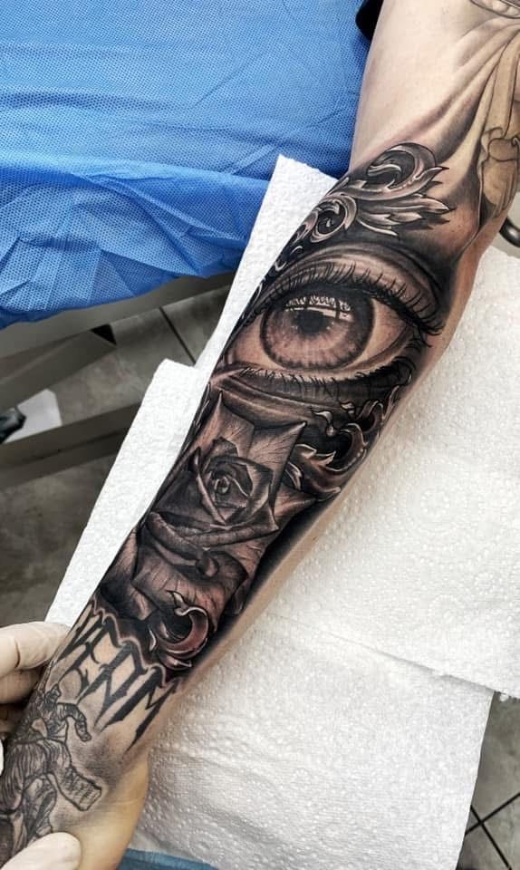 Detailed black and gray arm tattoo: eye, roses, ornate scrollwork. Tattoo is being worked on. — Whitsunday Tattooing Airlie Beach in Whitsundays, QLD
