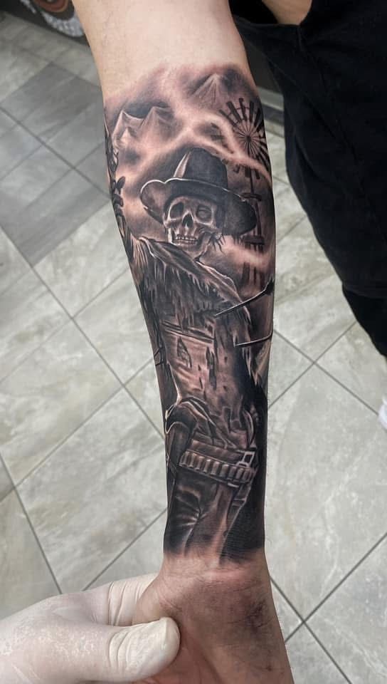Tattoo of a cowboy skeleton with a hat, gun belt, and a weathered building backdrop in black and gray. — Whitsunday Tattooing Airlie Beach in Whitsundays, QLD