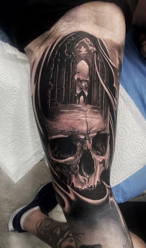 Black and gray skull tattoo on a leg, with a gothic archway and figure inside. — Whitsunday Tattooing Airlie Beach in Whitsundays, QLD