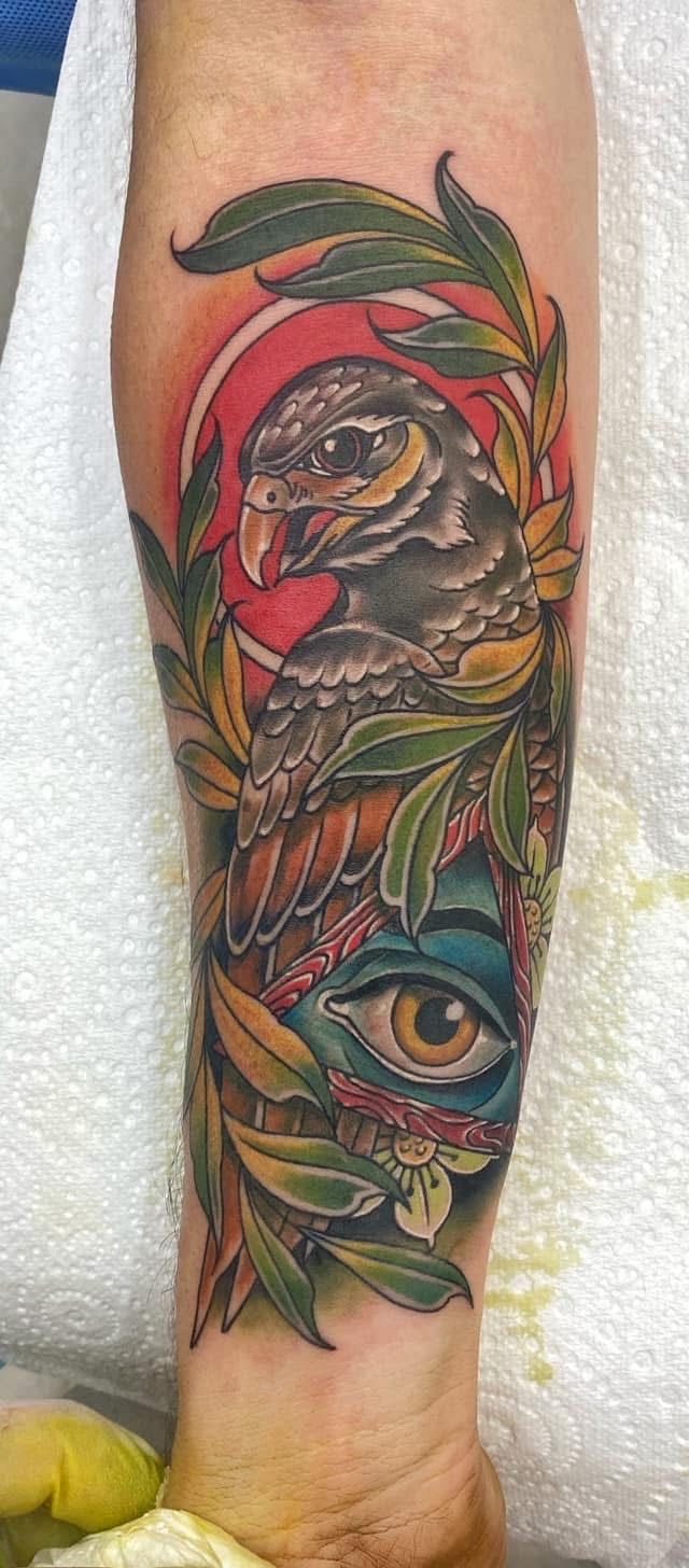 Tattoo of a hawk and an eye on an arm surrounded by leaves with red and blue tones. — Whitsunday Tattooing Airlie Beach in Whitsundays, QLD
