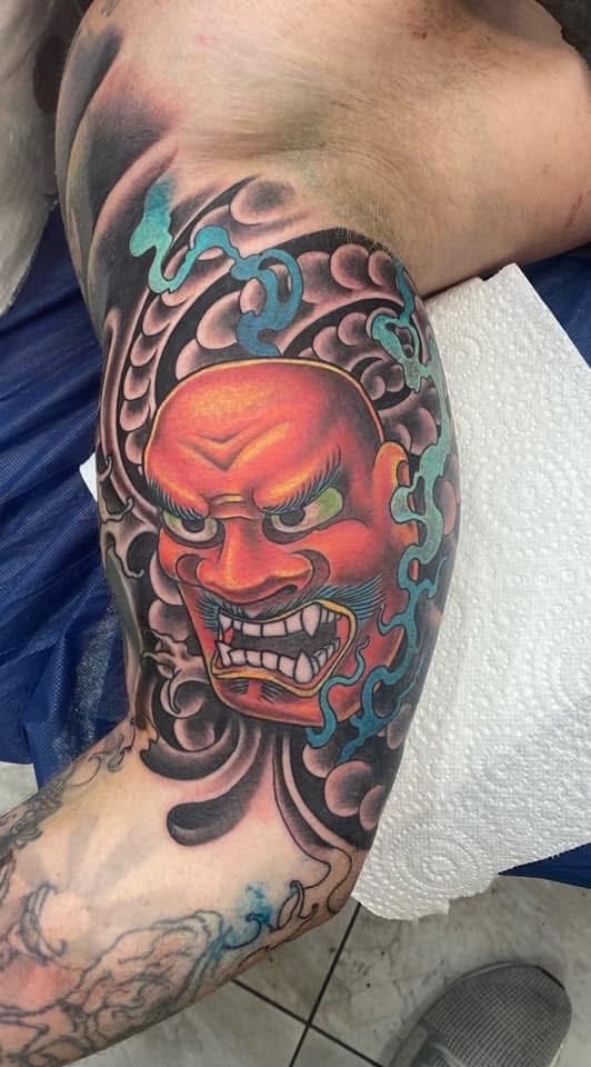 Japanese demon mask tattoo on arm, red and black with blue swirls. — Whitsunday Tattooing Airlie Beach in Whitsundays, QLD