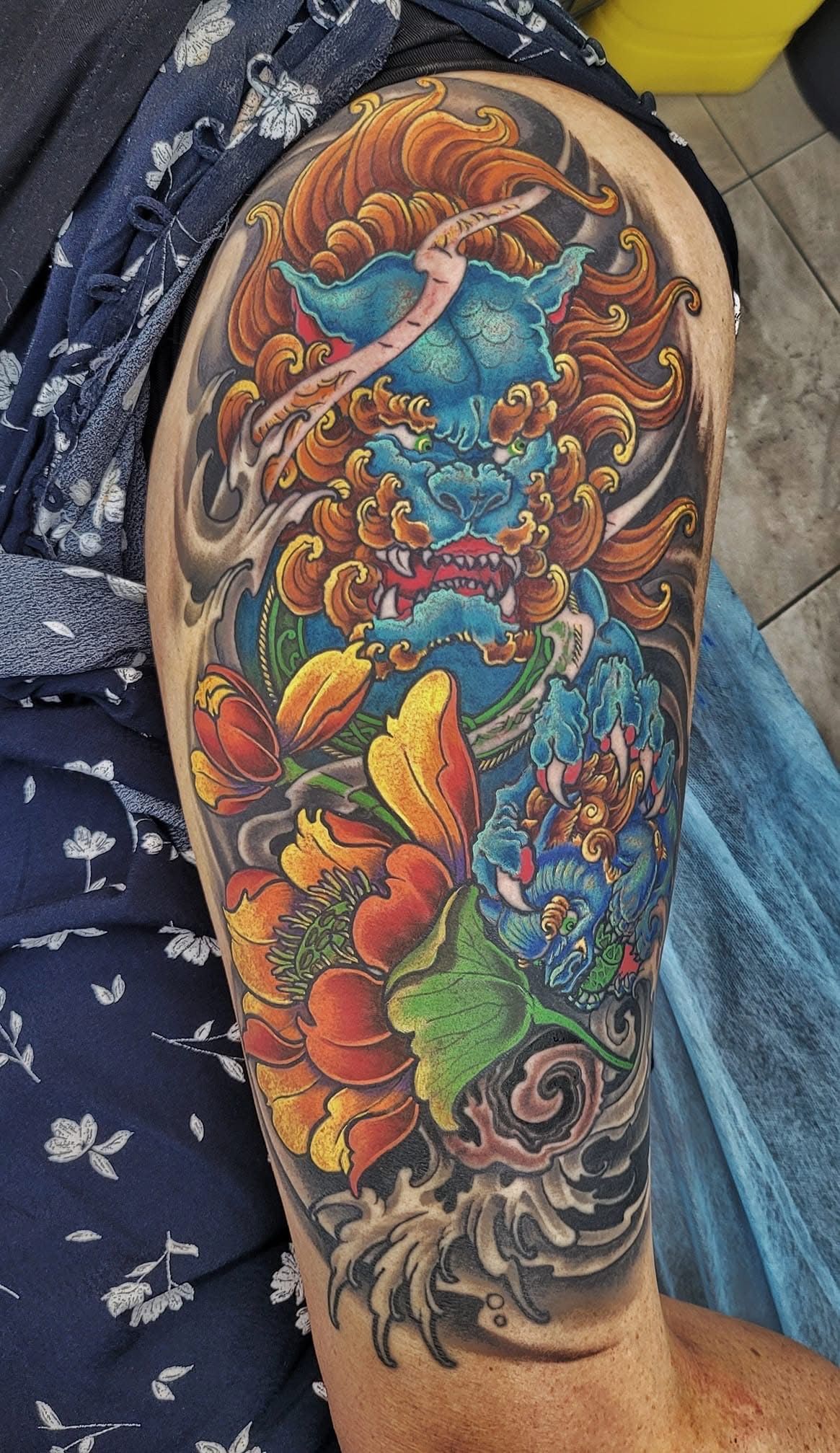 Colorful tattoo of a blue foo dog with a flame-like mane, flowers, and wave patterns on a person's arm. — Whitsunday Tattooing Airlie Beach in Whitsundays, QLD