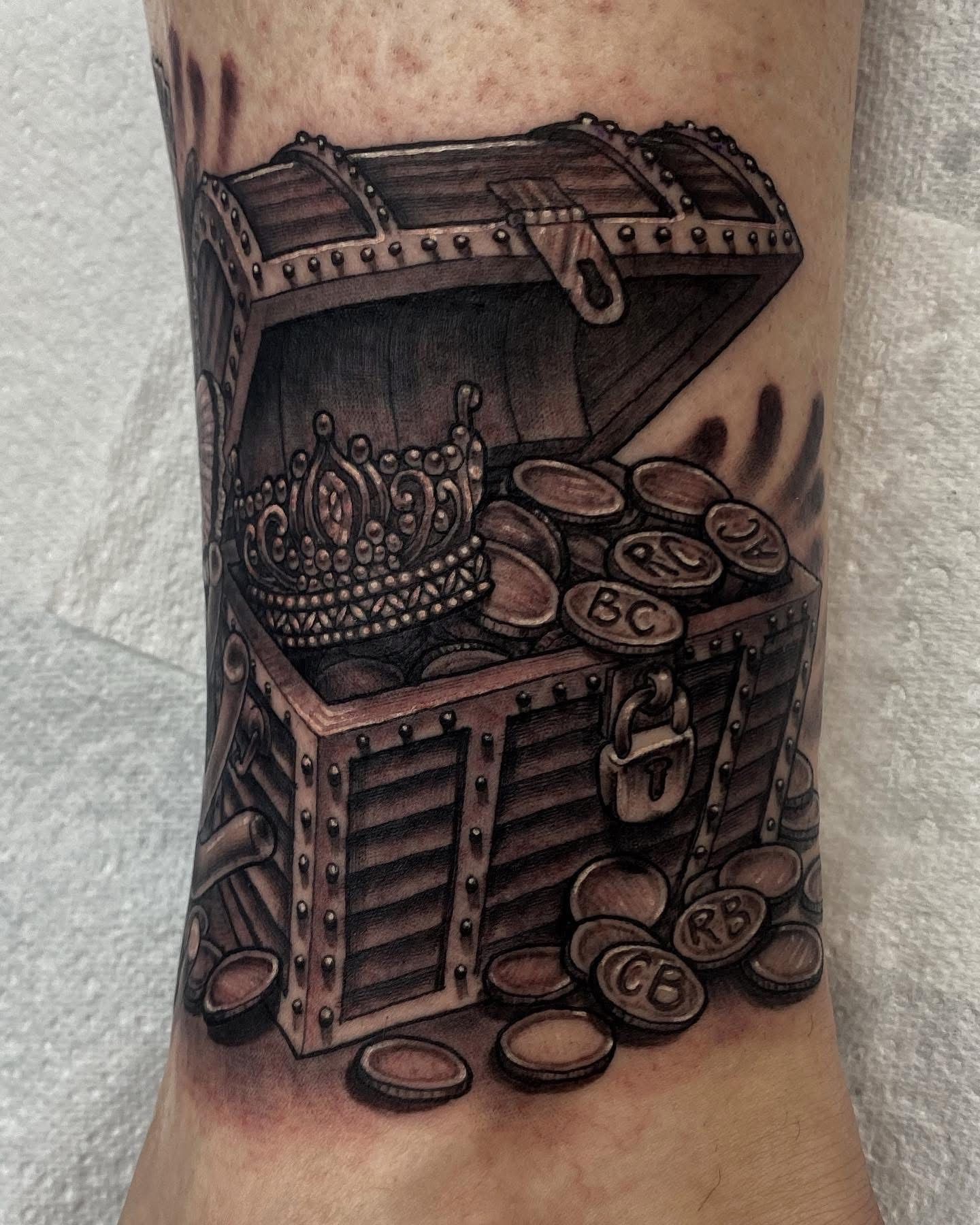Tattoo of an open treasure chest filled with coins and a crown on an ankle, shaded in grayscale. — Whitsunday Tattooing Airlie Beach in Whitsundays, QLD